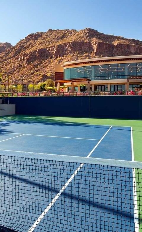 A blue hard court at a desert country club, with the clubhouse and mountain behind it.